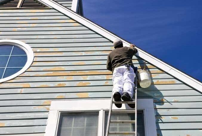 Schilder op ladder verft blauw huis.
